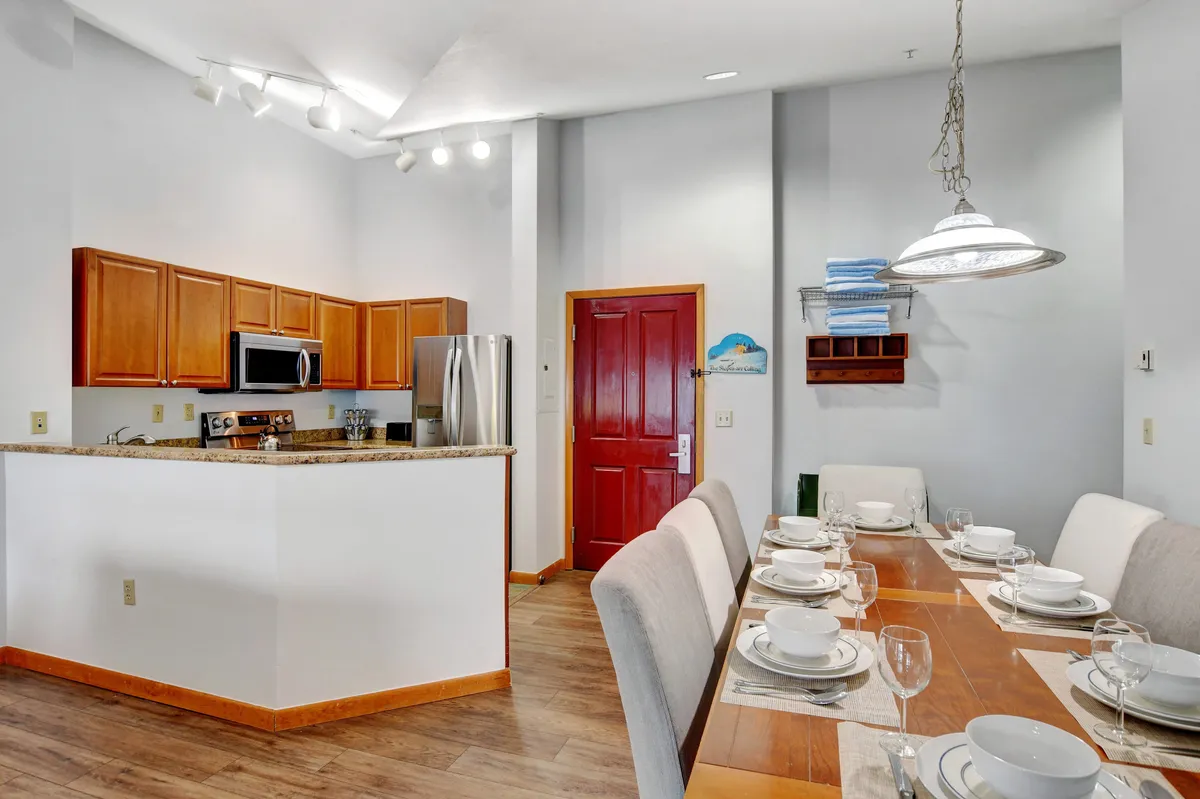 An elegant dining table is thoughtfully set for a meal, with the adjoining chef’s kitchen visible in the background. Stainless steel appliances, a bright and open layout, and the iconic red front door add a welcoming touch, ideal for hosting or enjoying family dinners.