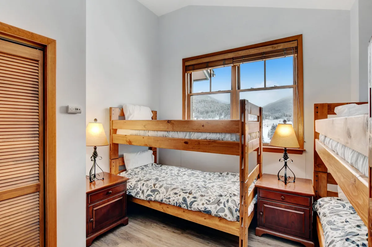A family-friendly bunkroom with bunk beds, a window with mountain views, and table lamps. The setting is cozy, playful, and perfect for kids or friends, encouraging memorable family moments.