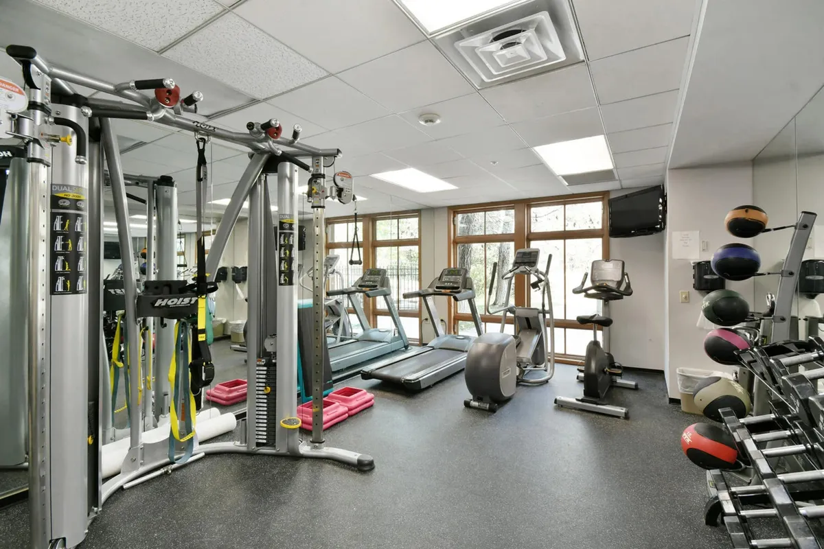 A bright, well-equipped fitness center with weight machines, treadmills, exercise mats, and free weights. The space is designed for both individual workouts and group fitness activities, with ample natural light and an invigorating atmosphere.