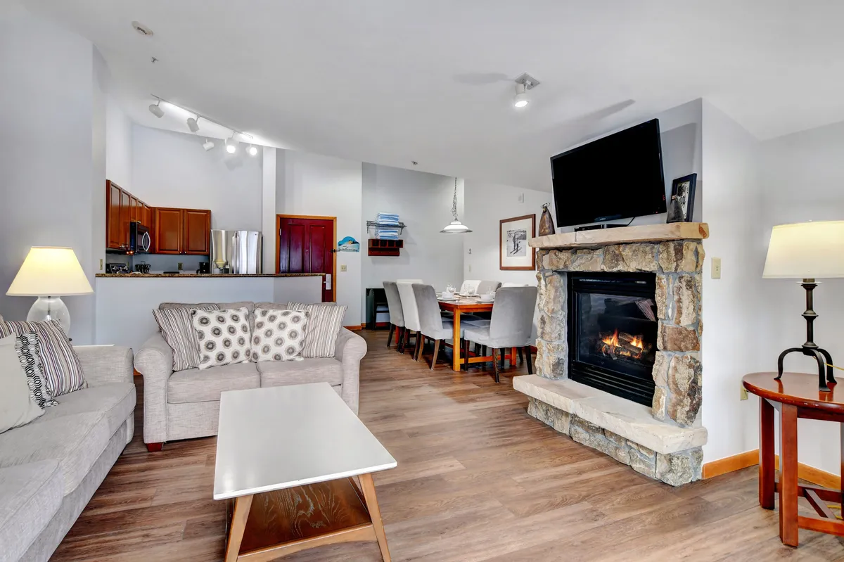 A warm and inviting open-concept space featuring a cozy fireplace, a plush sofa, and a spacious dining area. The glow of the fire and soft lighting create a relaxing atmosphere ideal for family gatherings, entertaining guests, or unwinding after a day on the mountain.