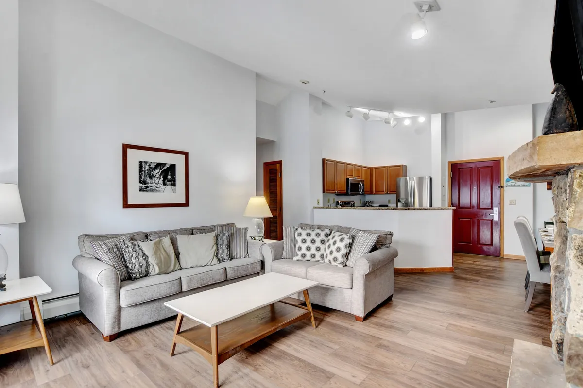 A spacious living area with a comfortable sofa, coffee table, and adjacent kitchen, adorned with tasteful artwork. The open-concept design is ideal for relaxing, entertaining guests, or enjoying family game nights.