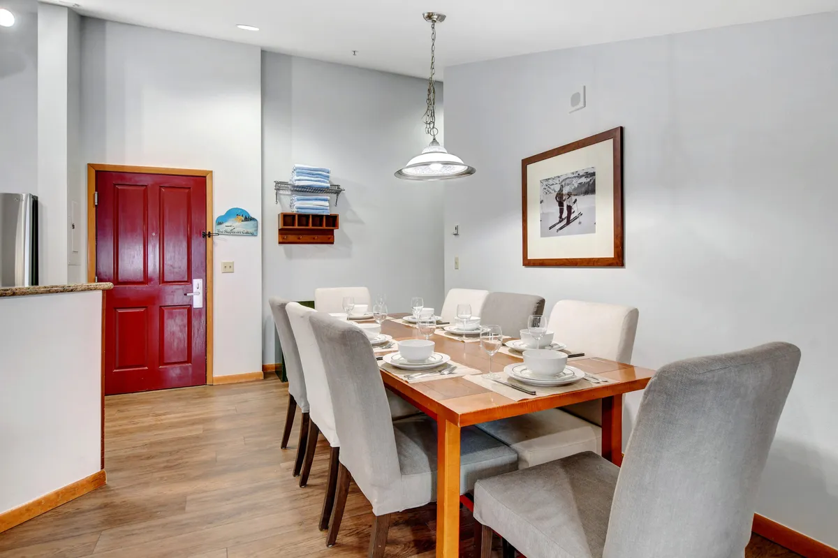 This image showcases a dining table set for a meal, with a warm, inviting atmosphere emphasized by the red front door and framed photograph on the wall. The setup evokes the feeling of family dinners, gatherings with friends, and the creation of memorable moments together.